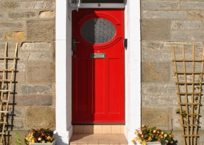 Red front door, with flowers in pots on either side.