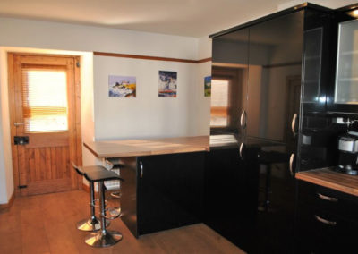 Breakfast bar with stools to the left of a kitchen; the units have a gloss black finish.