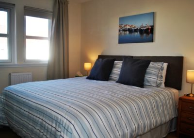 Super king size bed with lamps on bedside tables either side. Photograph of harbour scene above bed