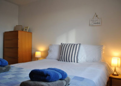 Double bed dressed in blue and white cotton, bedside tables create a warm glow