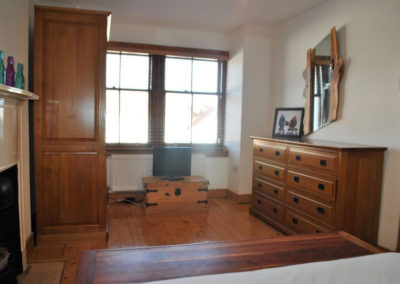 TV on a wooden box beneath a window. Large wooden chest of drawers and wardrobe sit either side.