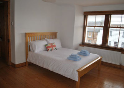 Double bed with white linen and union jack pillow beside a double window
