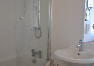 Bathroom tiled in white, shower over a curved bath