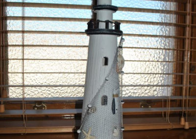 Model of a lighthouse, a fishing net is draped over it with shells and fish caught in it