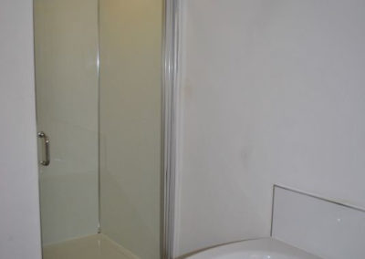 Shower with hinged door. In foreground is a corner bath