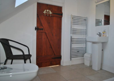 Bidet, chair and sink in bathroom with latched, wooden door