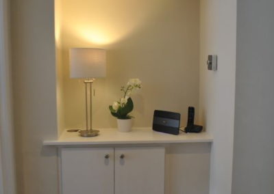 Alcove in hallway has a lamp, cupboard and telephone