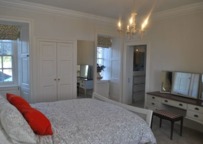 Bedroom with large bed, dressing table, windows and door through to en suite
