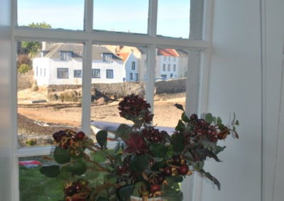 View of the beach through a window; a pot of flowers rests on the window sill