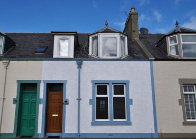Terraced house, painted blue with two dormer windows, a front door and a window.