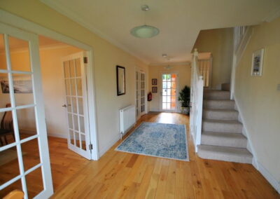 Wide, wooden floored hallway with double doors to left and stairs to the right.