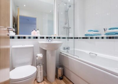 Tiled white walls, bath with shower, white bathroom suite
