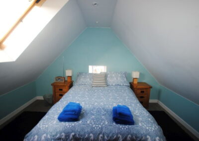 Double bed beneath sloped ceiling with a window on the left roof