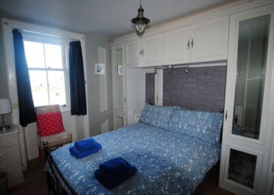 Double bed beneath cupboards unit, window on left