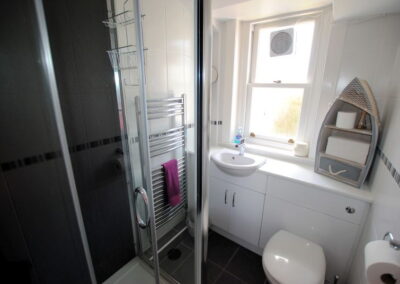 Shower on left, sink in front of window with extractor fan, boat-like shelves above toilet