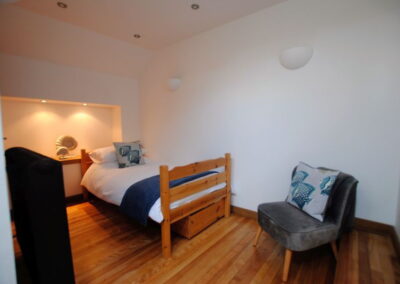 Single bed in corner of wooden floor room with lit alcove