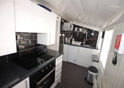 Black tiled kitchen with white cupboards and window on left.