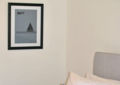 Painting of a boat on the wall beside the bed