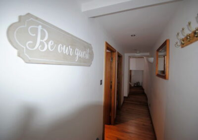 Corridor with sign reading Be our guest on wall opposite coat hooks