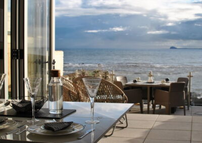 View through French doors to a patio with table and beyond that the sea