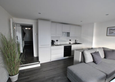 White kitchen units at the back wall of the lounge with grey, corner sofa
