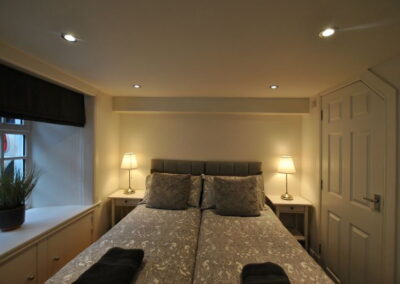 Looking from the bottom of the bed towards the headboard. White bedside tables either side with bedside lamps
