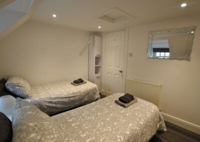 Beds beneath a sloped ceiling. A white unit behind the door. Mirror on wall opposite window.