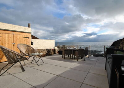 Patio area on two levels with bench and chairs at top and table and chairs nearer the sea.