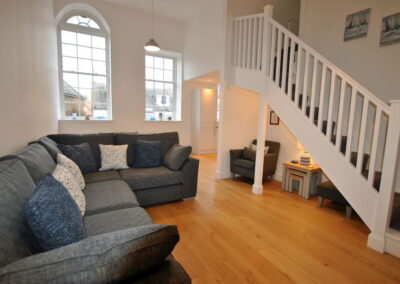 Open plan area with corner sofa, table beyond and wooden stairway up to first floor