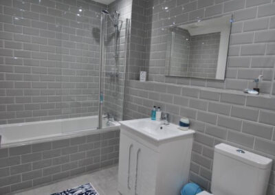 Grey, tiled bathroom with bath and shower and white fittings