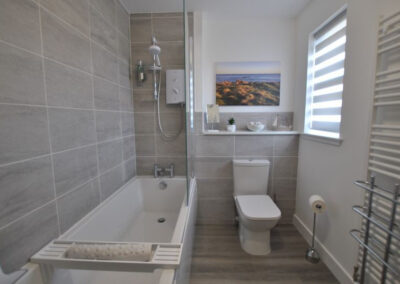 Tiled bathroom. Shower over bath, toilet and window.