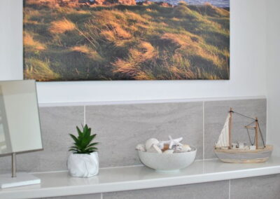 Large photograph on wall above shelf with plant, bowl of coastal artefacts and boat