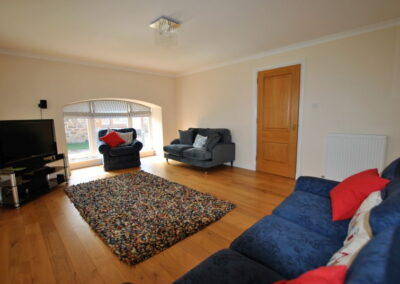 Large lounge with wooden floor, furniture around the room, TV unit and rug in the middle