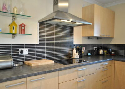 Kitchen units with light wooden effect, striped black and white tiles, chrome extractor hood