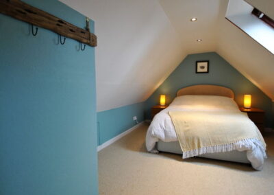Bed beneath sloped ceiling, with Velux window. Lamps on bedside tables either side of bed.