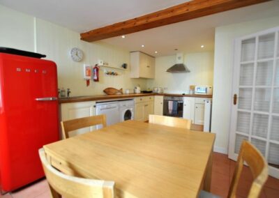 Wooden table in middle of kitchen with four chairs. Large, red Smeg fridge