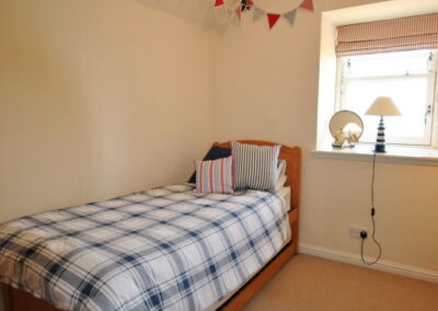 Single bed with checked linen, beneath bunting. Window behind bed.