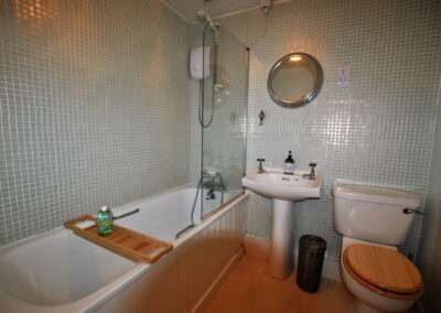 Tiled bathroom with white suite, wooden toilet seat, and shower over bath