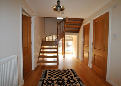 Wide hallway with wooden floor. Wooden steps curve upwards to the right.