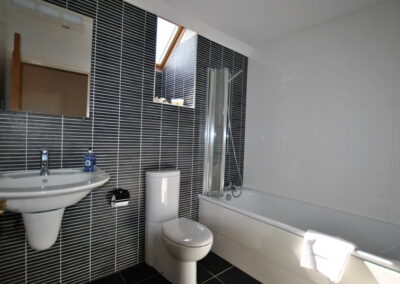 White bathroom suite with shower over the bath and large square mirror over sink