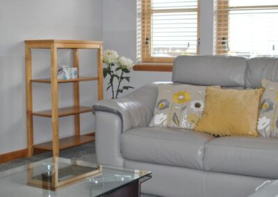 Grey leather sofa next to free-standing shelf unit and flowers