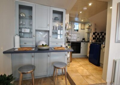 Grey units with breakfast bar and two four-legged stools. To the right is a step up to the kitchen.