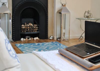 A laptop on a laptop table in the foreground, in the background is a fireplace