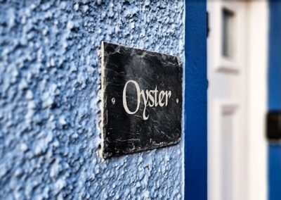 Close-up of Oyster sign next to front door on blue harling wall