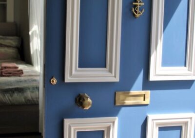 Sunlight on the white and blue front door. The door has an anchor door knocker.