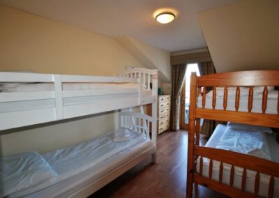 White wooden bunk beds to the left, warm wooden bunks ot the right. A door to the balcony at the end of the room