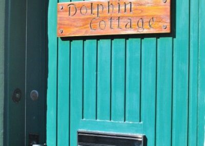 Turquoise front door with sign that reads Dolphin Cottage