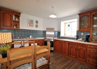 Wooden fitted kitchen with stove and washing machine opposite a dining table