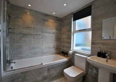 Tiled bathroom to the ceiling. Shower over white bath