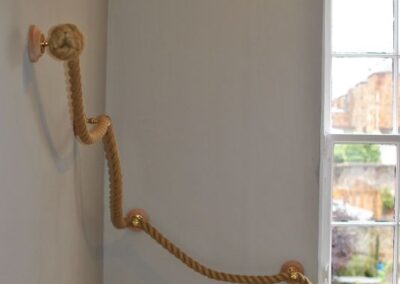 Rope bannister curves down stairs to the right past a large window